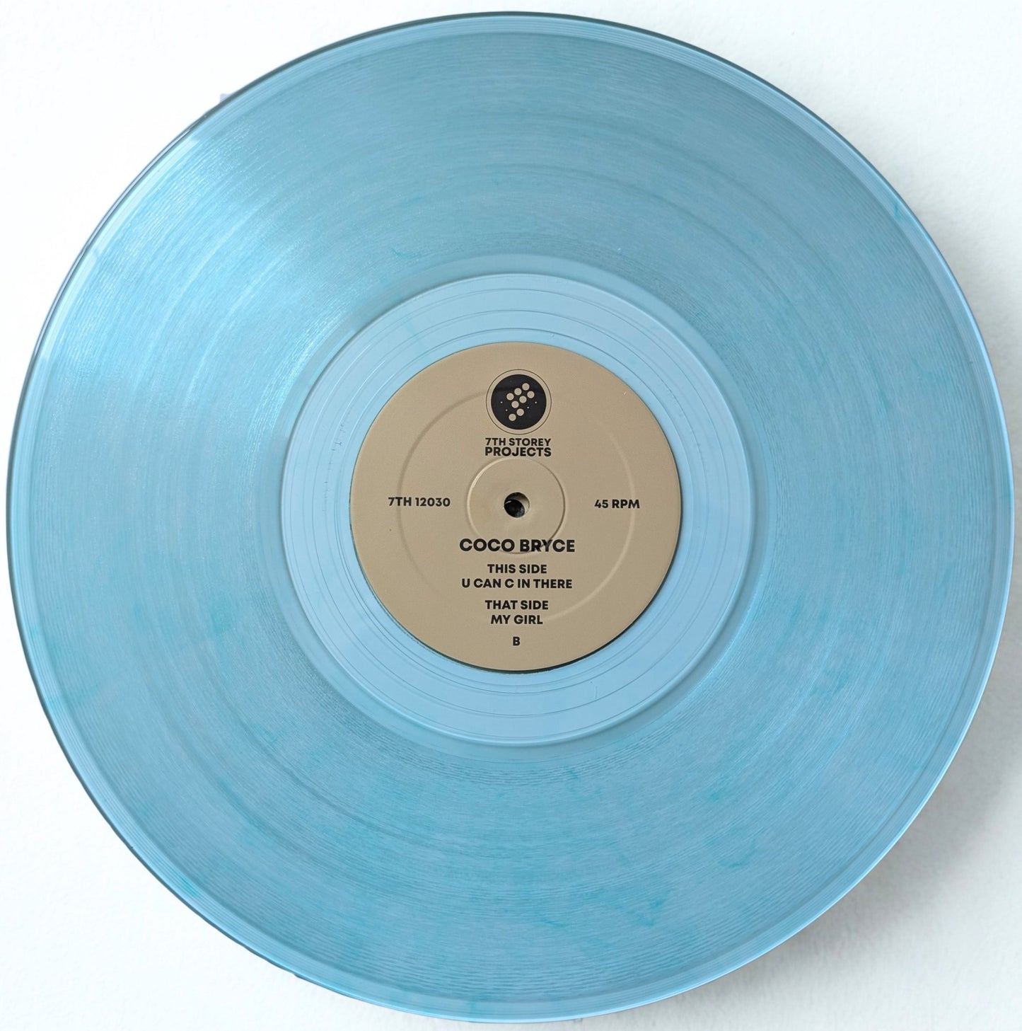 A light blue translucent vinyl record with a beige center label reading Coco Bryce, photographed from above against a plain white background.