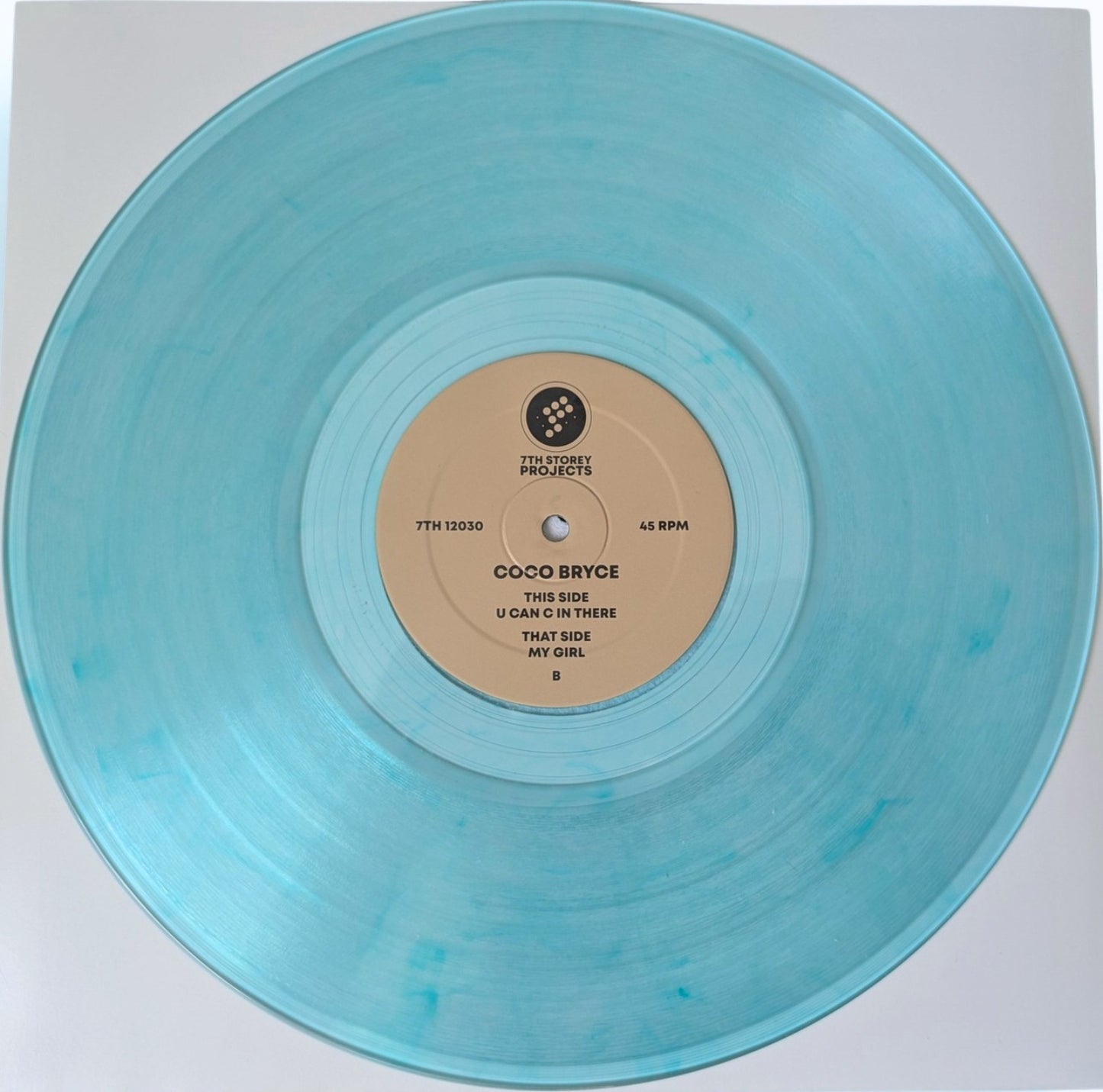 A translucent light blue vinyl record with a beige center label, photographed from above on a white background. The label reads Coco Bryce and includes the track title 'U Can't In There That Side My Girl'.