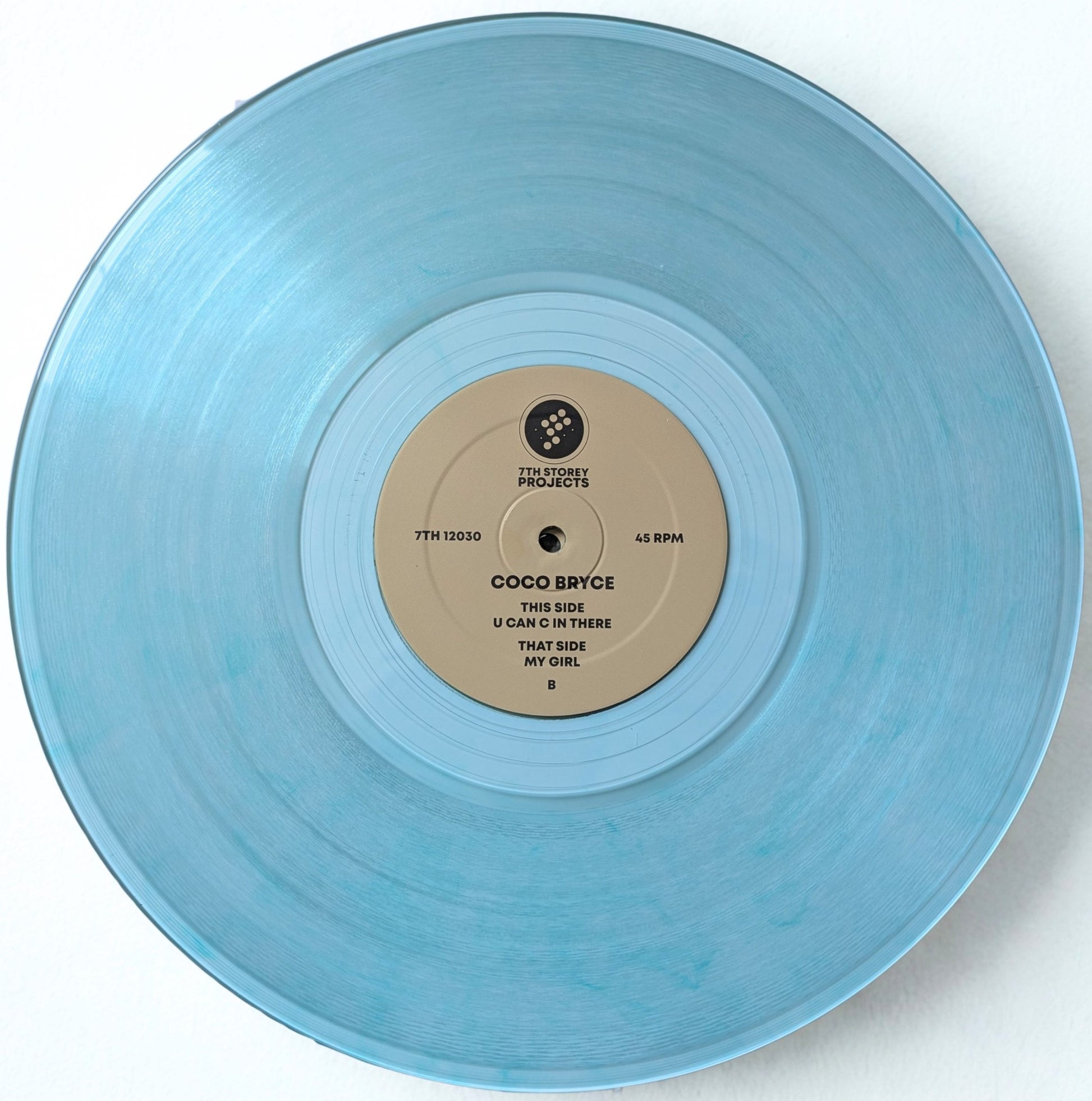 A light blue translucent vinyl record with a beige center label reading Coco Bryce, photographed from above against a plain white background.