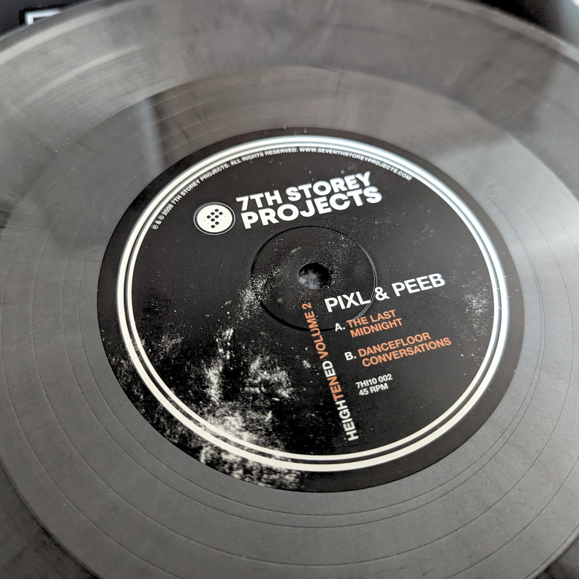 A close-up of a vinyl record with a black center label reading '7th Storey Projects' and the track title 'Pixl & Peeb', photographed on a dark surface.