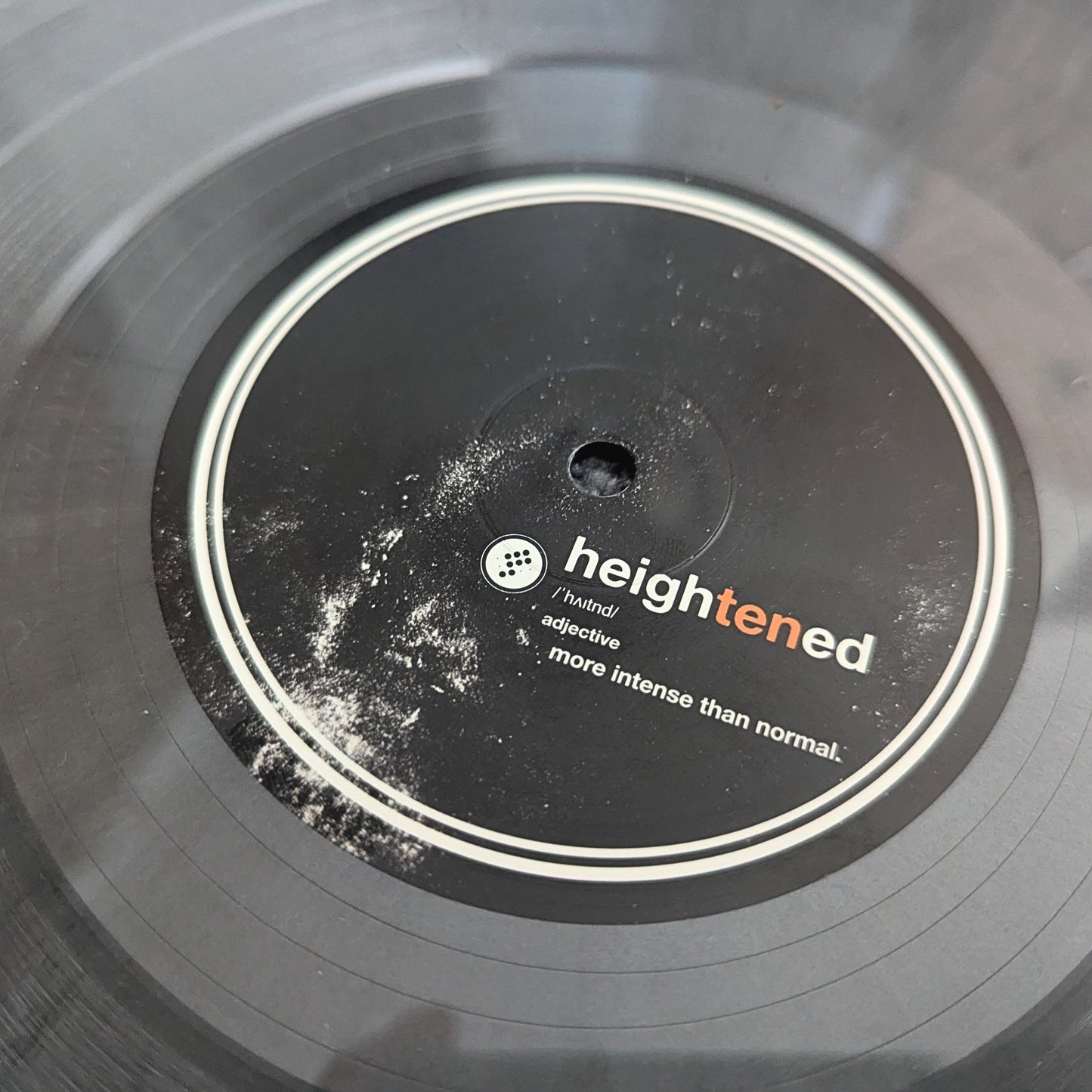 Close-up of a vinyl record label reading 'heightened' with smaller text 'intensive' and 'more intense than normal.' on a dark gray/black record.